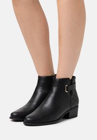 Bottines en cuir noir avec un bout carré, un dos en textile matelassé et un détail en boucle dorée. Talon carré bas.