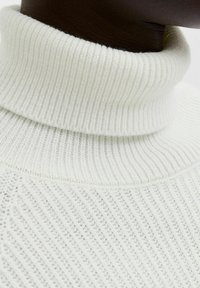 Suéter blanco de cuello alto con textura acanalada, que presenta un cuello alto y un patrón de punto en diagonal a lo largo de la tela.