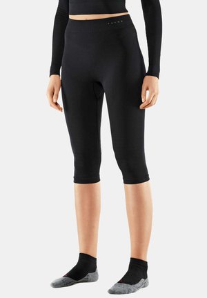 Zwarte knielange leggings van rekbaar materiaal met een ribbelstructuur. De tailleband is voorzien van een logo. Ggedragen met zwarte en grijze sokken.