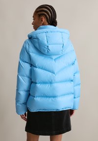Helles blaues Puffer-Jacke mit Kapuze, mit Chevron-Nähten, dicker Polsterung und gerippten Bündchen, kombiniert mit einem dunklen Rock.