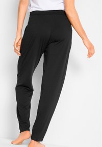 Pantaloni in tessuto morbido e nero con vestibilità morbida e vita elastica. Il design presenta cuciture piatte e polsini all'altezza della caviglia leggermente arricciati.