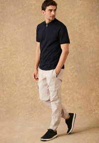 Polo a maniche corte blu navy con colletto a zip, abbinato a pantaloni cargo beige chiaro con tasche e sneakers nere con suola bianca.