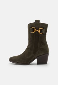 Stivaletto in suede verde oliva con punta affusolata, ritagli decorativi e hardware in tono oro con un accento a doppio anello. Design con tacco a blocco.