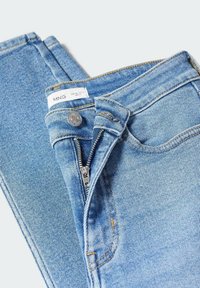 Jean en denim bleu clair avec une braguette à fermeture éclair standard, un bouton en métal argenté et des coutures apparentes. Le tissu a une texture lisse.