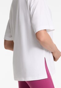 Hvid bomulds T-shirt med korte ærmer, split sider og lige kant, parret med højtaljede lyserøde leggings.