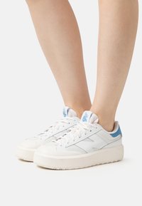 Białe trampki z jasnoniebieskimi akcentami, z teksturowaną cholewką, podwyższoną gumową podeszwą i tradycyjnym zapięciem na sznurowadła.
