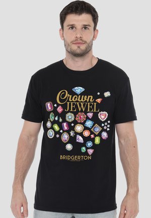 Mann trägt schwarzes T-Shirt mit bunter Juwelen-Grafik und dem Text „Crown Jewel Bridgerton“ auf der Vorderseite vor einfachem Hintergrund.