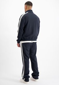 Marine sportieve trainingsoutfit met witte strepen, bestaande uit een jack met rits en broek met elastische band. Zachte stof en een relaxed fit.