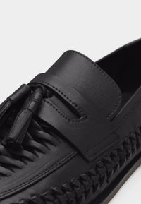 Czarna skórzana mokasyna z plecionymi detalami i frędzlami z przodu, z przeszywanymi krawędziami i gładkim wykończeniem.