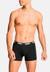 Schwarze Baumwoll-Boxershorts mit einer engen Passform und einem weißen PUMA-Logo am Bund. Glatte Textur, knielang.