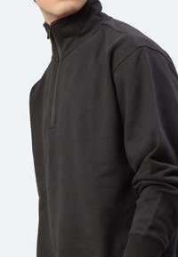 Schwarzer Fleece-Pullover mit hohem Kragen und halbem Reißverschluss. Weiche Textur, lockere Passform, gerippte Bündchen und Saumdetails.