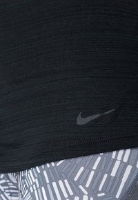 Top ajustado de Nike en negro, con tejido texturizado y un pequeño logo. Combinado con leggings estampados en gris y blanco, que presentan líneas verticales.
