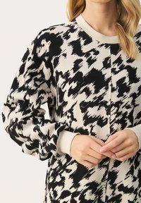 Svart och vit mönstrad tröja, med rundad halsringning, ribbade ärmslut och en mjuk textur. Designen inkluderar abstrakta penseldragsmotiv.