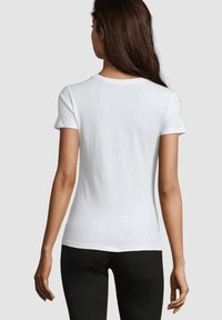 Camiseta de algodón blanca con mangas cortas y corte entallado, con escote redondo y textura suave. Se muestra vista trasera.