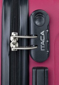 Maleta rosa con herrajes negros, que cuenta con dos cremalleras metálicas, un candado de combinación y un exterior texturizado. Los detalles incluyen una placa con el logotipo.