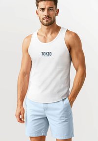 White tank top with "TOKIO" printed in dark blue, paired with light blue shorts. The fabric appears smooth with a casual fit.