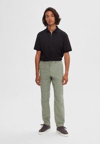 Polo negro con cremallera y mangas cortas, combinado con chinos verde claro y zapatillas grises. Diseño simple, ajuste cómodo, minimalismo en los detalles.