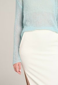 Light blue, sheer knit sweater with long sleeves, paired with a fitted white skirt featuring a thigh-high slit on one side.