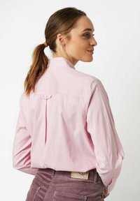 Light pink, striped long-sleeve shirt with a collar and a back pleat detail. Features a button closure at the neck. Soft fabric texture.