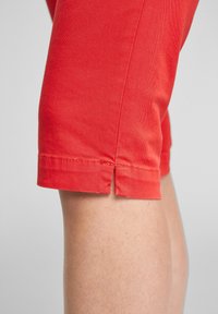 Pantalones cortos de algodón rojos con un diseño ajustado, que presentan una abertura lateral en el dobladillo y detalles de costura visibles. La tela tiene una textura suave.