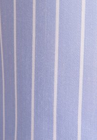 Tissu bleu clair avec des fines rayures blanches verticales régulièrement espacées, montrant le détail de la texture et du tissage.