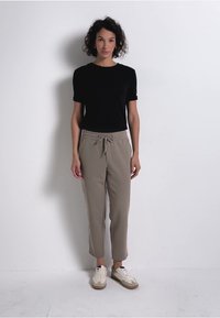 Zwarte T-shirt met korte mouwen, beige joggerbroek met trekkoord en crèmekleurige sneakers met bruine accenten. Eenvoudige, casual outfit.