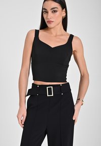 Top corto nero aderente con spalline larghe e scollatura a V, abbinato a pantaloni neri a vita alta con una grande fibbia rettangolare.