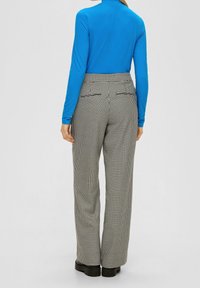 Blauwe lange mouwen top gecombineerd met zwart-witte houndstooth-patroon broek, met een recht silhouet en achterzakken. Zwarte schoenen maken de look compleet.