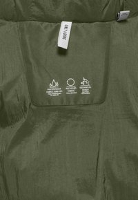 Notranjost olivno zelene jakne z gladkim, vodoodpornim materialom. Ima oznake, ki nakazujejo na reciklirane materiale in tehnično obdelavo.