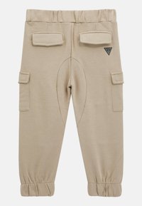 Beżowe dziecięce spodnie dresowe z elastycznym pasem i mankietami, z kieszeniami nakładanymi na udach i biodrach, z małą trójkątną naszywką z logo.