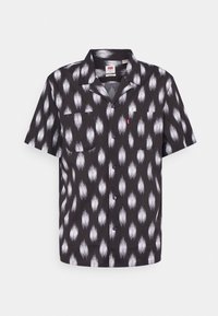 Camisetta nera a maniche corte con motivo astratto bianco, colletto a punta, taschino frontale e chiusura a bottoni. Realizzata in tessuto leggero.