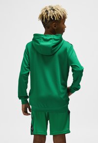 Grøn hættetrøje i tekstureret stof, kombineret med grønne shorts med sorte detaljer, set bagfra.