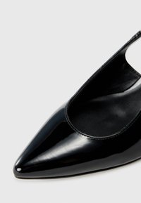 Black patent leather pointed-toe shoe with a cut-out design and smooth texture. Interior features a soft black lining.