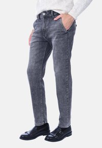 Jeans in denim grigio con vestibilità slim, dotati di tasche anteriori, chiusura con bottone e cuciture a contrasto sui lati. Abbinati a scarpe nere.