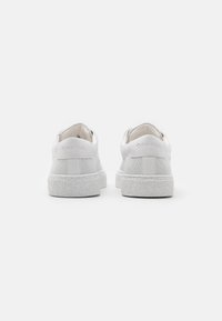 Zapatillas blancas con piel suave y acentos texturizados, con suela de goma y branding en relieve en el talón.