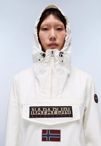 Weiße, leichte Jacke mit hohem Kragen und verstellbarem Kapuzen. Schwarzes Markenlogo und norwegisches Flaggen-Patch auf der Vorderseite. Glatte Gewebestruktur.