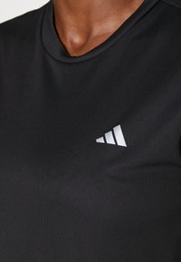 Czarna sportowa koszulka o gładkiej fakturze, z okrągłym dekoltem i białym logo Adidas z ukośnymi paskami po lewej stronie.