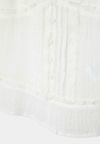 Tissu blanc avec plis verticaux, petits boutons recouverts de tissu et détails en dentelle le long du centre et des bords inférieurs.