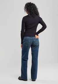 Black ribbed long-sleeve top with fitted waist paired with blue straight-leg jeans featuring back pockets and a faded wash.