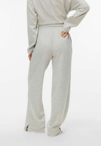 Gaisas pelēkas sporta bikses ar vaļēju piegriezumu, izgatavotas no mīksta auduma, ar sānu šķēlumiem apakšmalā un gludu vidukļa joslu ērtībai.