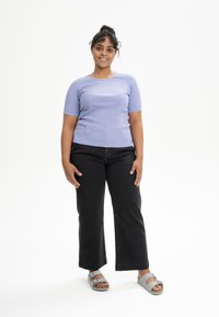 Lichtpaarse geribde top met korte mouwen, zwarte Wide-leg jeans, grijze sandalen met banden, model staat met ontspannen handen langs de zijkanten.