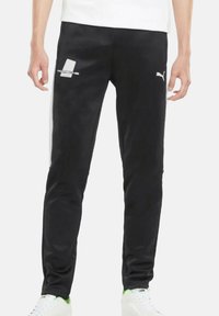 Schwarze Trainingshose mit schmaler Passform. Aus glattem Material gefertigt, mit weißen Akzenten und einem Logo auf dem linken Oberschenkel.