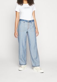 Jasnoniebieskie, szerokie dżinsy z guzikami i przeszyciami. Połączone z białą koszulką z czarnym napisem.