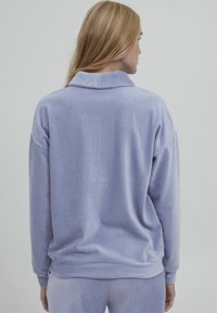 Lila Velours-Sweatshirt mit Kragen, lockerer Passform und gerippter Textur. Verfügt über fallende Schultern und eine glatte Oberfläche.