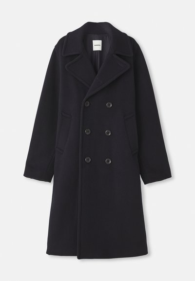 Dviejų eilių tamsiai mėlynas vilnos paltas su dideliais iškirptais atvartais, keturiais priekiniais mygtukais ir dviem šoninėmis kišenėmis. Klasiško tiesaus kirpimo dizainas.