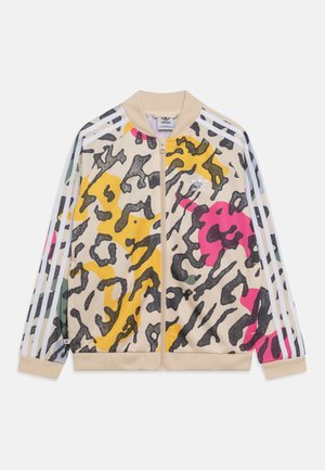 Beige Adidas Reißverschlussjacke mit buntem abstraktem Tierdruck in Gelb, Pink, Schwarz und Grün, mit weißen drei Streifen an den Ärmeln.