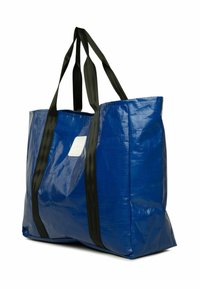 Zila tote somiņa, kas izgatavota no spīdīga, izturīga materiāla. Tai ir melnas rokas un baltā etiķete vienā pusē. Taisnstūra forma ar ietilpīgu iekšpusi.