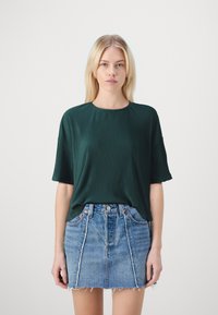 Mørkegrønn ribbestrikket t-skjorte med korte ermer, kombinert med en lys blå denimminiskjørt med slitt nederkant og frontlommer.