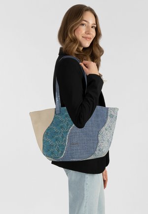Grand sac fourre-tout avec des panneaux en denim bleu et textile floral, doté d'une base beige. Agrémenté de coutures et de poignées confortables.