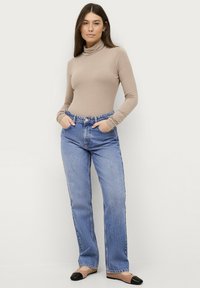 Beige Rollkragenpullover mit langen Ärmeln, kombiniert mit hellblauen, hoch taillierten gerade geschnittenen Jeans. Schwarze Ballerinas runden das Outfit ab.